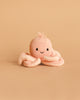 The Cuddle + Kind Baby Octopus (Soft Coral Pink), a hand-knit heirloom toy made from Peruvian cotton yarn with a smiling face, rests on a plain beige background.