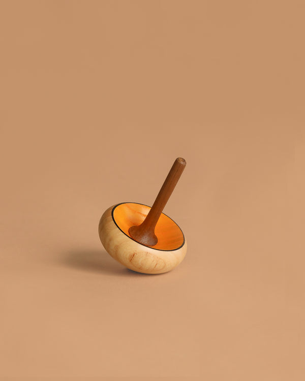 The Mader Zwirbel Spinning Top - Yellow, crafted in Austria, features a light beige body with an orange inner rim and is shown resting on its side against a plain light brown background.