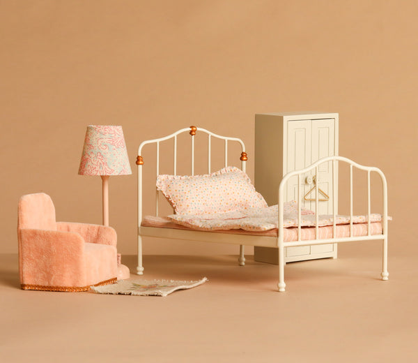 Maileg Bedroom Set featuring delightful Maileg mouse furniture, including a vintage-inspired white metal bed with patterned bedding, a small wardrobe, pink armchair, lamp, and rug—all beautifully displayed on a beige background.
