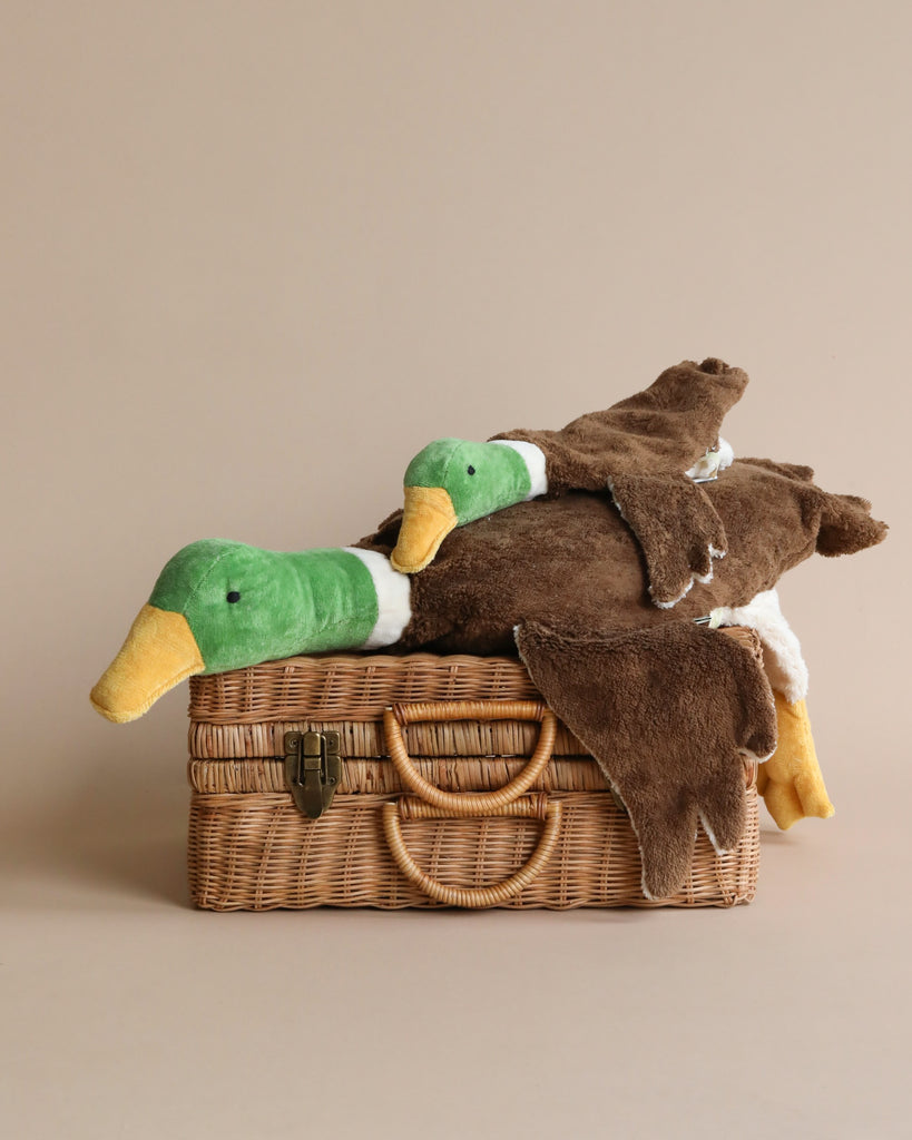 Two Senger Naturwelt Mallard ducks made from organic cotton resting on an open woven wicker picnic basket against a beige background.