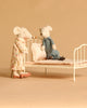 Two stuffed toy mice from the Maileg Bedroom Set with Grandma & Grandpa are shown beside a small white Maileg Vintage Bed. The Grandma Mouse, dressed in a floral nightgown, stands beside the bed, while Grandpa Mouse in blue pajamas sits on the bed facing her.
