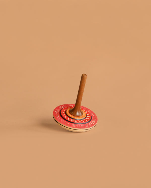 The Mader Bonbon Spinning Top - Orange features a wooden design with an orange, embossed pattern disc and a brown handle, shown against a plain beige background.