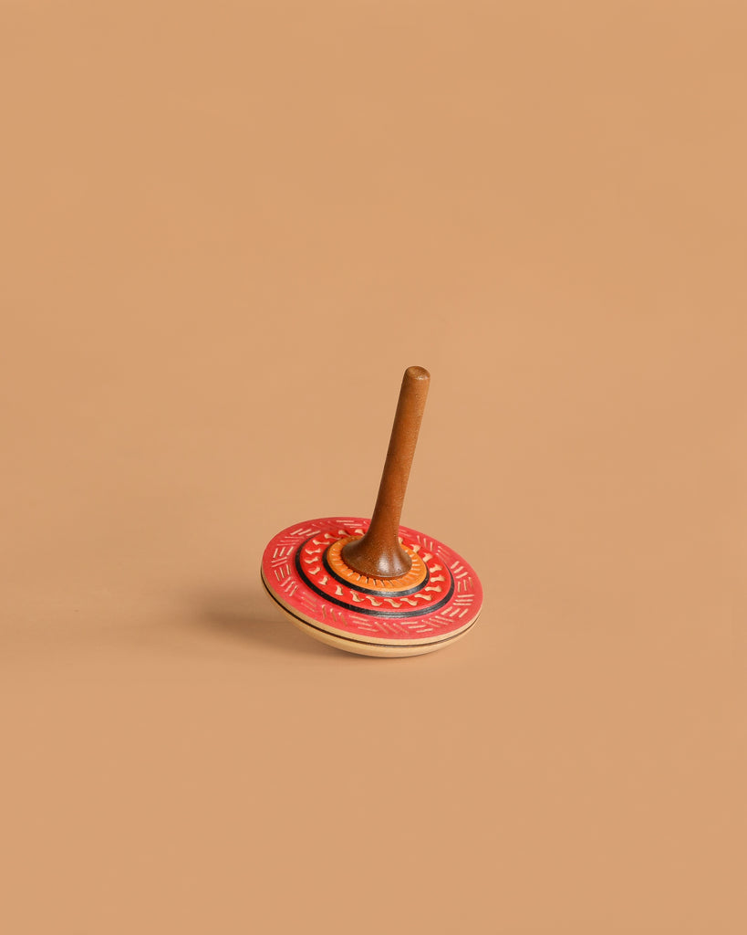 The Mader Bonbon Spinning Top - Orange features a wooden design with an orange, embossed pattern disc and a brown handle, shown against a plain beige background.