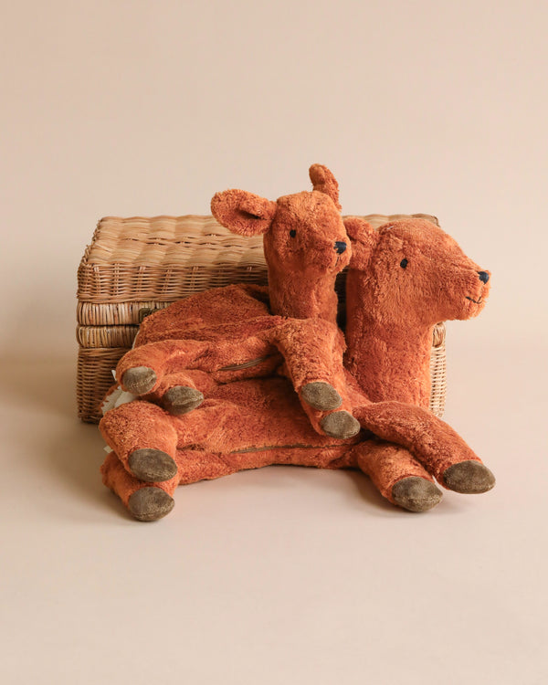 Two well-loved, plush Senger Naturwelt Cuddly Animal - Deer toys sitting against a wicker basket on a neutral background. The toys appear old with visible wear and faded fabric, suggesting they are