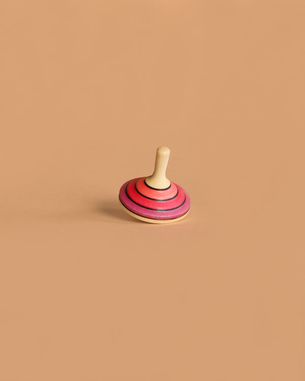 The Large Mader Tango Spinning Top in magenta, made from maple wood, stands upright on a plain light brown surface with a minimal background.