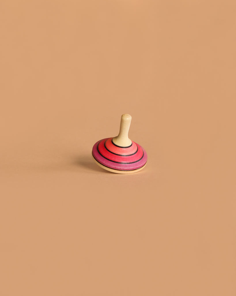 The Large Mader Tango Spinning Top in magenta, made from maple wood, stands upright on a plain light brown surface with a minimal background.