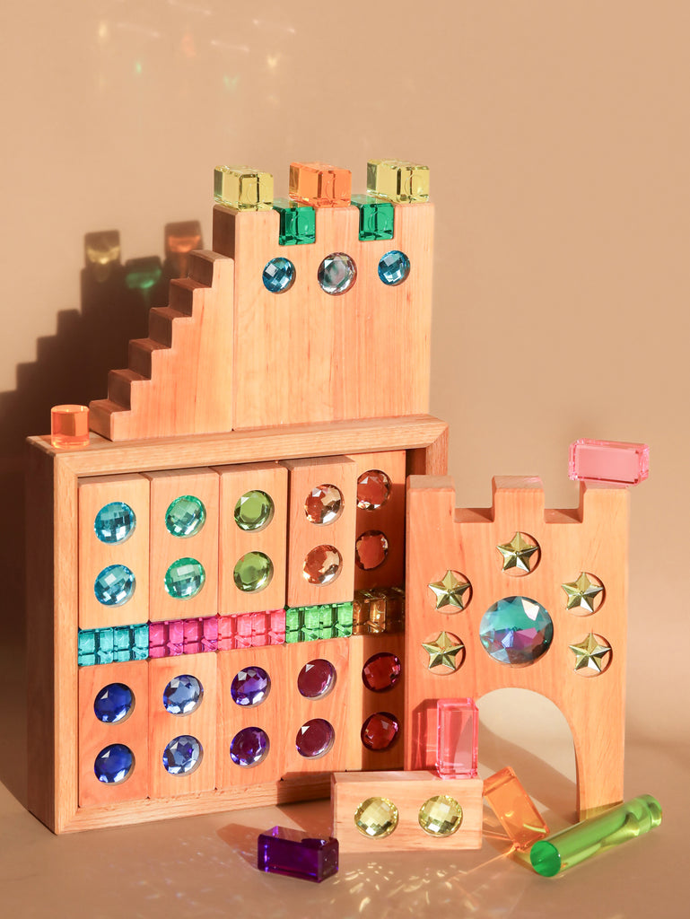 The Bauspiel Gem Blocks with Pastel Lucent Cubes (45 pieces) are assembled into a castle featuring arches, steps, and a tower. Vibrant gem-like insets enhance its appearance against a neutral background.