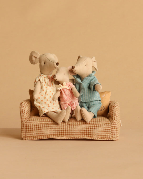 The Maileg Family Time Set features three stuffed toy mice—Mum and Dad Mice with the Little Sister Mouse sitting between them—arranged on a small checkered Maileg couch against a plain beige backdrop. The Little Sister Mouse is dressed in pink, while Mum and Dad wear blue and white outfits with orange dots.