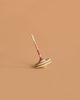 The Mader Spaghetti Spinning Top - Pink, crafted from maple wood, is balanced upright on a plain, light brown surface.