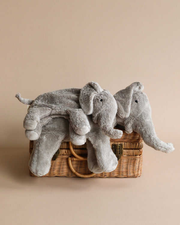 Two Senger Naturwelt Cuddly Animal - Elephant plush toys nestled in a wicker basket against a plain beige background. The elephants appear soft and cuddly, with one lying on top of the other.