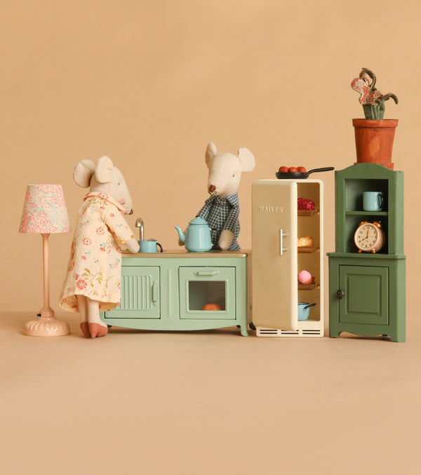Grandma and Grandpa Maileg mice enjoy a cozy time at home in a delightful miniature kitchen, featuring the Maileg Kitchen Set with pastel stove, open fridge, cabinet, lamp, and potted plant—all set against a beige background.