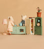 Grandma and Grandpa Maileg mice enjoy a cozy time at home in a delightful miniature kitchen, featuring the Maileg Kitchen Set with pastel stove, open fridge, cabinet, lamp, and potted plant—all set against a beige background.