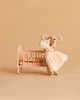 The Maileg Big Sister and Me Nursery Set features a plush mouse in a dress holding a smaller lace-wrapped mouse, both standing beside a pink cradle with a patterned mattress, set against a plain beige background.