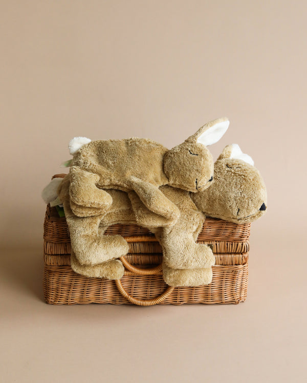 Two Senger Naturwelt Cuddly Animal - Rabbit toys made from organic cotton laying on top of a wicker basket against a beige background. One bunny appears to be asleep, draped over the other.