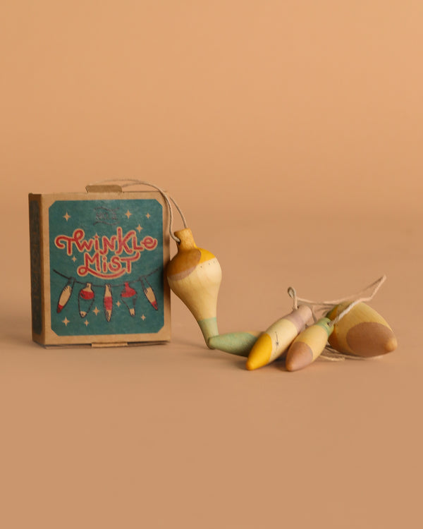 A small Grapat Ornament Set - Twinkle Mist sits by four pastel wooden fishing bobbers tied with string—charming handmade ornaments ideal for holiday décor—arranged on a beige background.