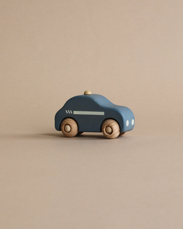 A simplistic wooden police car crafted from responsibly sourced beech wood, painted in dark blue with visible wood grain rotating wheels and minimalistic white detailing, positioned on a smooth beige background.