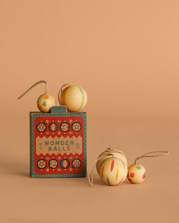 The Grapat Ornament Set - Wonder Balls features colorful wooden balls, some with string loops for hanging, presented in a vintage-style box against a neutral beige background.