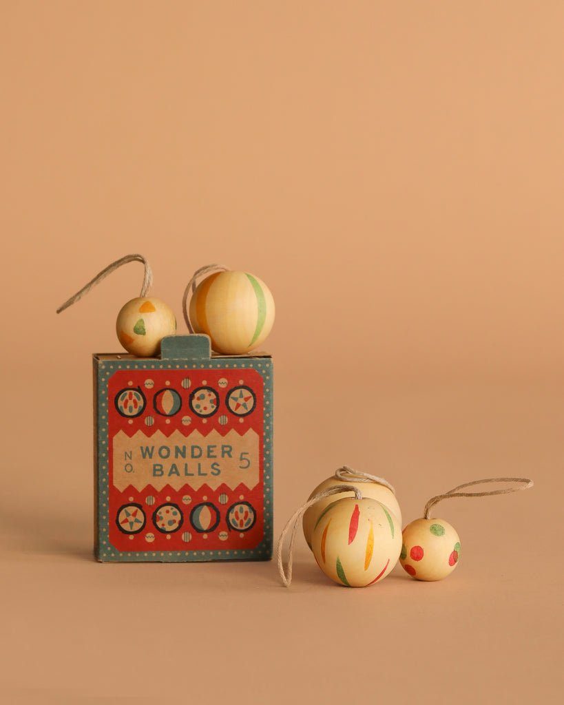 The Grapat Ornament Set - Wonder Balls features colorful wooden balls, some with string loops for hanging, presented in a vintage-style box against a neutral beige background.