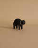 A small, hand-painted black figurine of a cat stands on a beige background. The cat has a simple and minimalist design with white eyes and a small white snout.