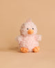 The Steiff Pipsy Pink Chick, a fluffy, light pink stuffed animal with an orange beak and feet, sits against a plain beige background.