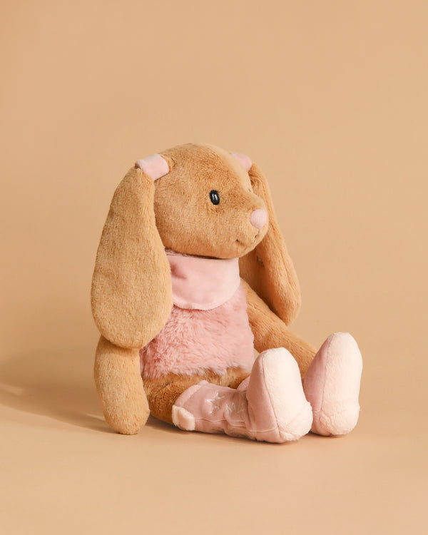 The Steiff Cowgirl Hoppie Rabbit, a plush bunny with floppy ears, light brown fur, and pink accents on its ears, chest, and feet, sits upright against a beige background—a perfect cuddly toy for any collection.