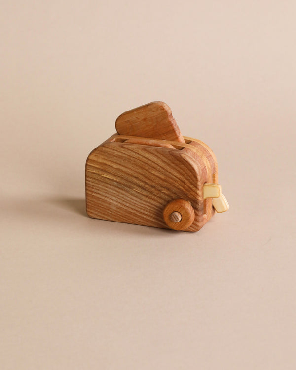 A handmade wooden toaster, with visible grain and a movable button on a plain beige background.