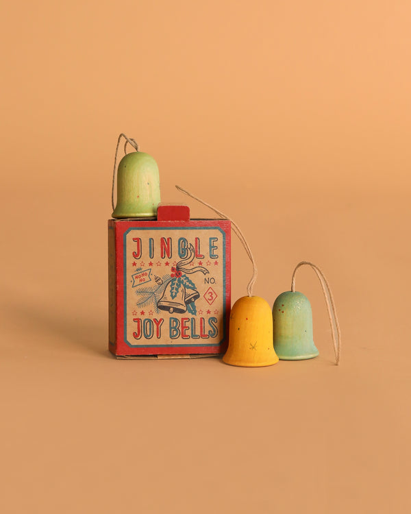 The Grapat Ornament Set – Jingle Joy Bells features a vintage red box and three hand-painted pastel ornaments in green, yellow, and blue, all displayed on a beige background for charming holiday décor.
