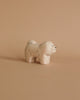 A Handmade Tiny Wooden Animals - Chow Chow Dog with simplistic, rounded features is set against a light brown background. Carved from Albizia wood, the dog has a small tail, short legs, and a content expression, with minimal black lines for facial features and body details.