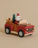 A Santa-mobile Music Box, crafted from premium hardwoods and painted in red and brown, features a snowman driver, a Christmas tree, and gifts, set against a beige background.