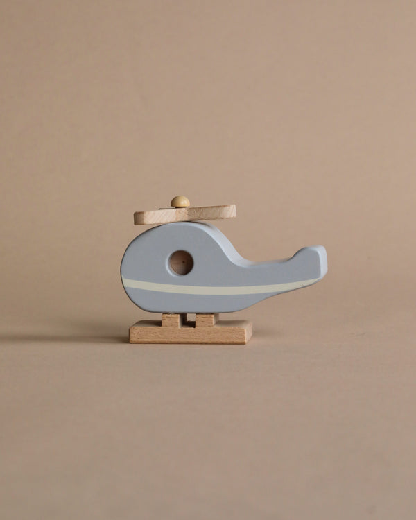 A Wooden Helicopter shaped like a bird in pale blue and natural wood colors, crafted from responsibly sourced beech wood, standing on a small wooden base against a neutral beige background.
