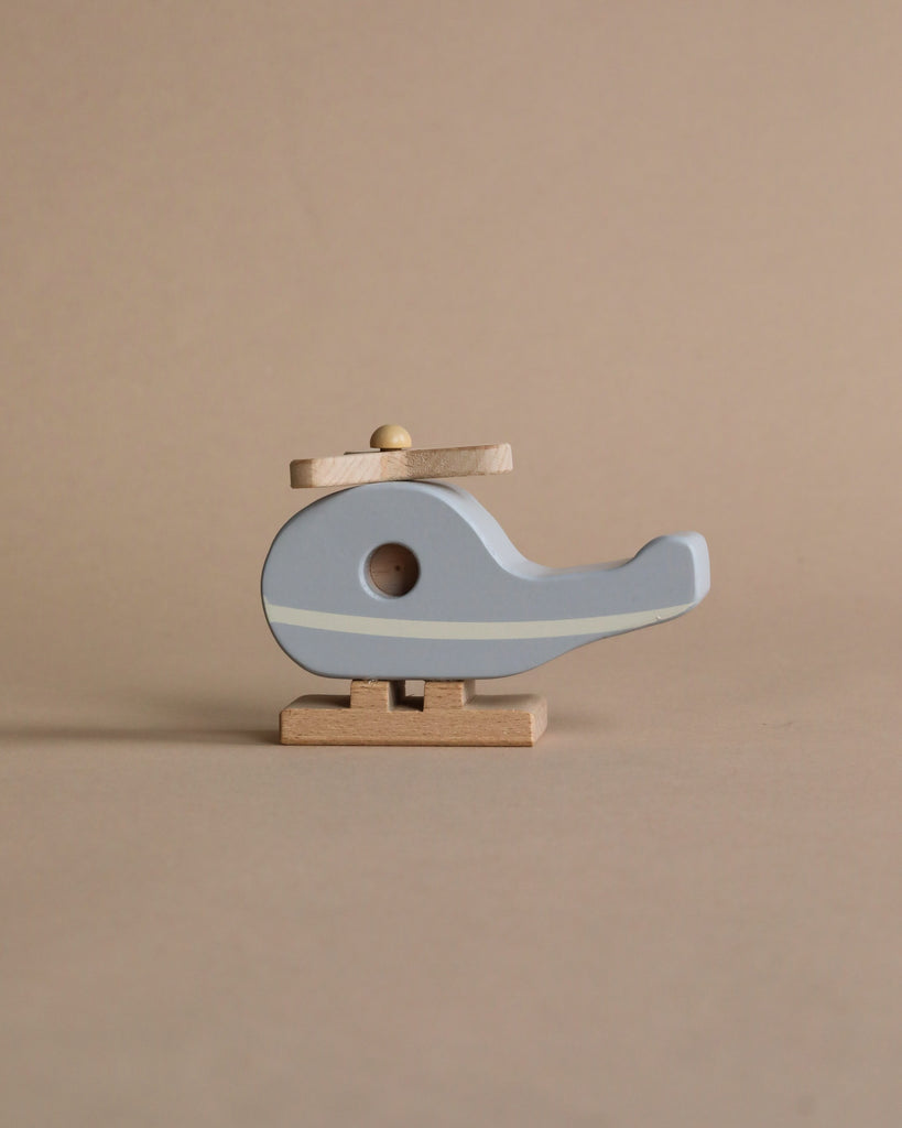 A Wooden Helicopter shaped like a bird in pale blue and natural wood colors, crafted from responsibly sourced beech wood, standing on a small wooden base against a neutral beige background.