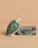 The Tiny Turtle Travel Set features a handmade felt turtle with a green shell, resting its front legs on a micro Maileg suitcase against a beige background.