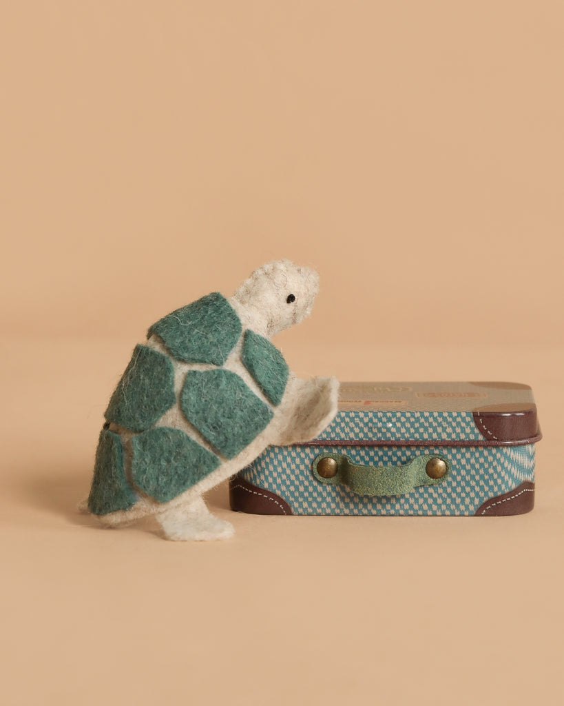 The Tiny Turtle Travel Set features a handmade felt turtle with a green shell, resting its front legs on a micro Maileg suitcase against a beige background.