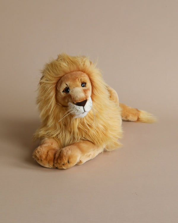 A Steiff, Leo Lion Plush Toy, crafted by Steiff toys with a full, fluffy mane and the signature Button in Ear, lies down against a plain beige background. The lion has a friendly expression and detailed facial