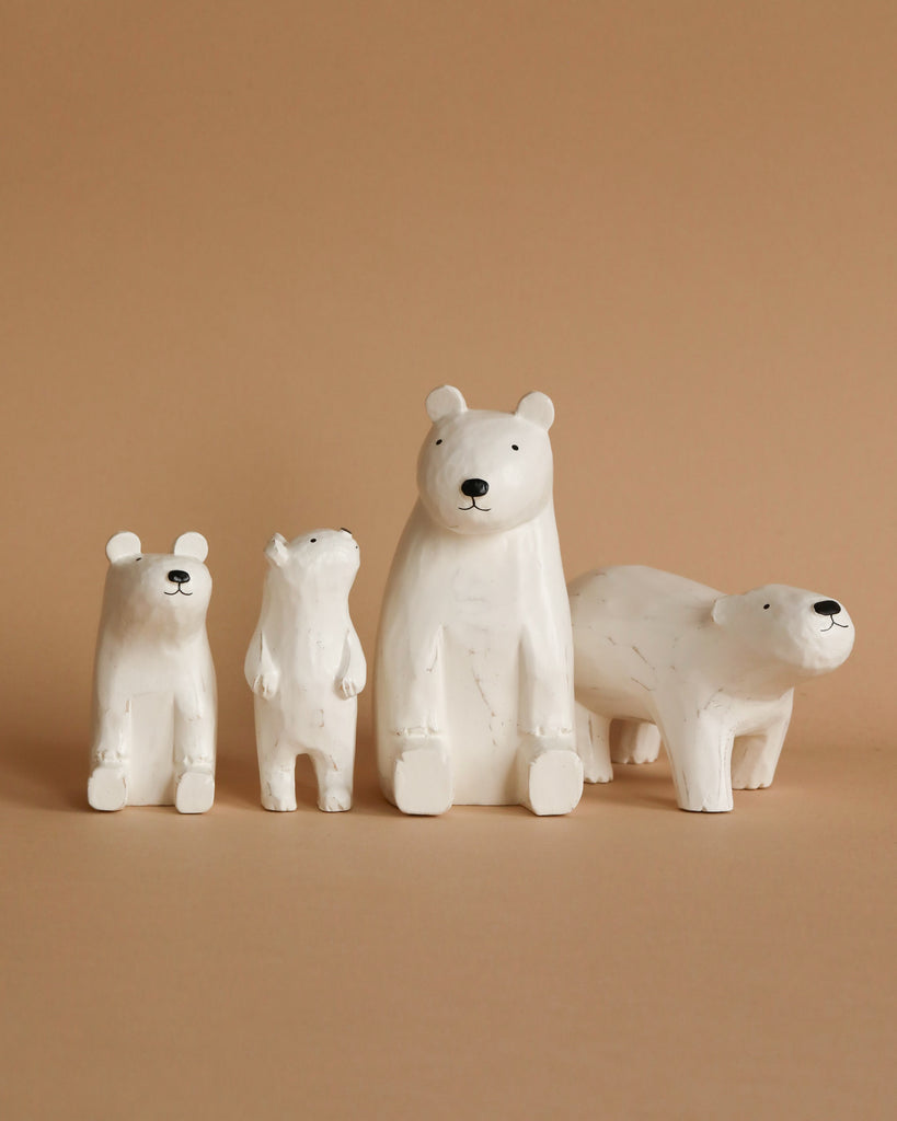 A lineup of four Handmade Tiny Wooden Polar Bears against a beige background. The figurines vary in size and pose, with one standing upright, one sitting, one mid-walk, and one crouched down.