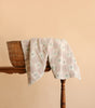 A woven basket with the Organic Cotton Baby Blanket - Fleur, featuring a light floral pattern, drapes gracefully over it on a wooden table against a plain beige background. Made in Portugal, this beautifully crafted blanket offers both comfort and quality for your little one.