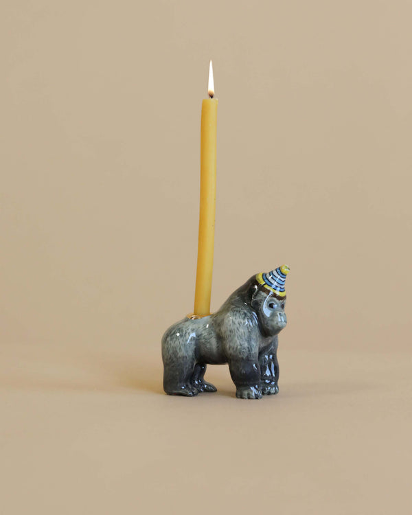 A hand-painted, ceramic Gorilla "Celebrate Nature" Cake Topper with a lit yellow taper candle on top, set against a plain beige background.