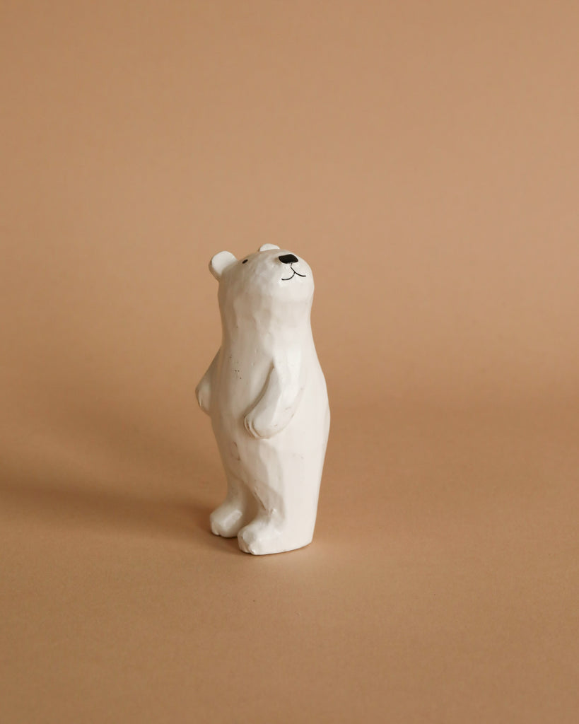 A Handmade Tiny Wooden Polar Bears stands upright on a light brown surface against a similar light brown background. The minimalist design, with simple black details marking its nose, eyes, and mouth, evokes the charm of handcrafted wooden animals.