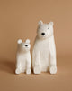 A photograph of two Handmade Tiny Wooden Polar Bears against a beige background. The larger, hand-painted polar bear sits to the right, and the smaller one sits to the left. Both bears have simple facial features and are positioned facing forward.