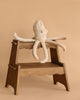 The Senger Naturwelt Cuddly Animal - Octopus, made from organic cotton with long floppy arms, rests on a wooden step stool against a beige background—an ideal calming companion for cozy moments.
