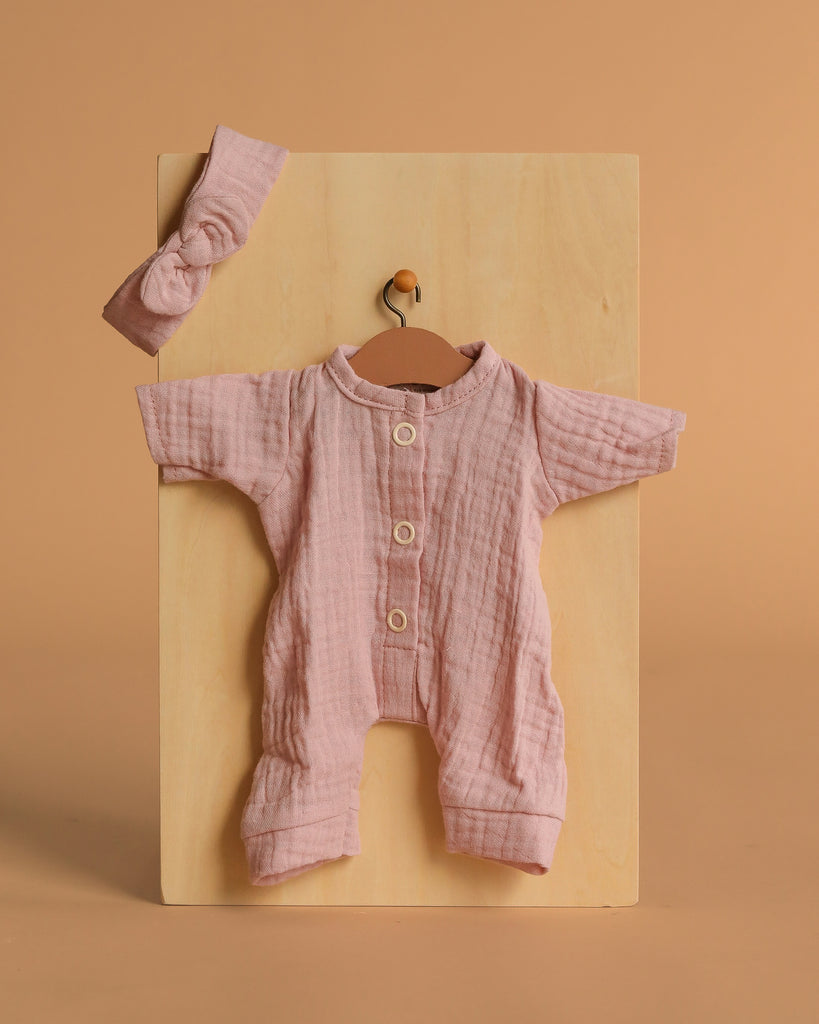 The Minikane 11" Doll Clothing set features the Lili Jumpsuit & Headband in Orchid Pink cotton gauze, displayed on a wooden board against a beige background—perfectly sized for Minikane dolls.