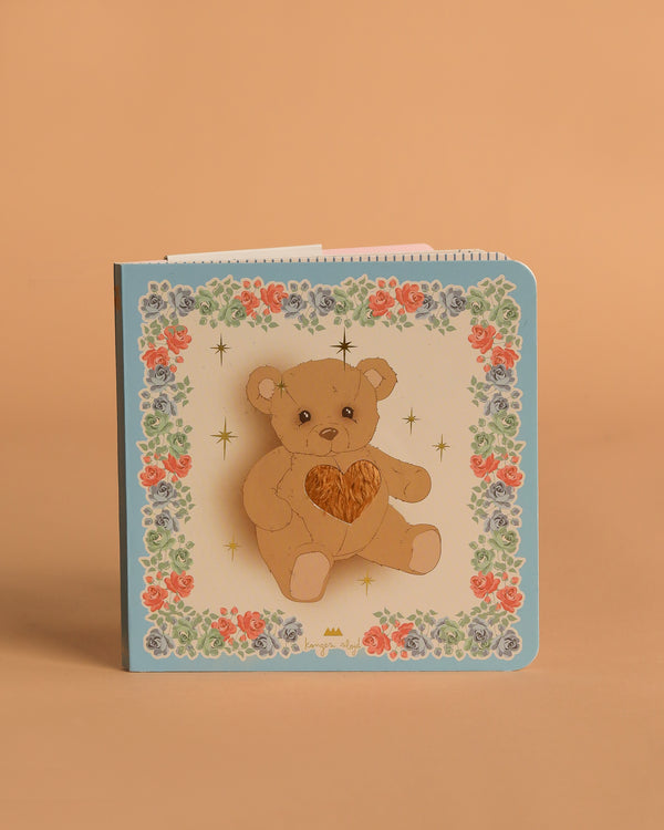 The Konges Sloejd Touch and Feel Book features a teddy bear with a heart, colorful floral borders, and gold stars on an FSC-certified, light background.