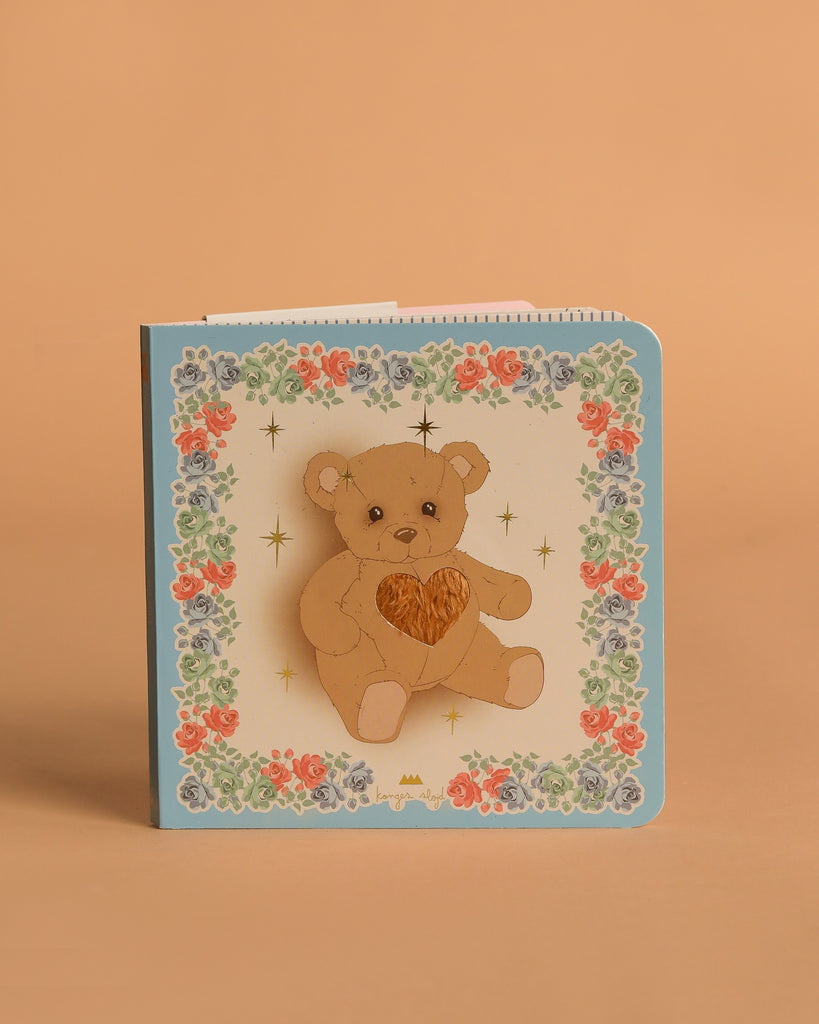 The Konges Sloejd Touch and Feel Book features a teddy bear with a heart, colorful floral borders, and gold stars on an FSC-certified, light background.