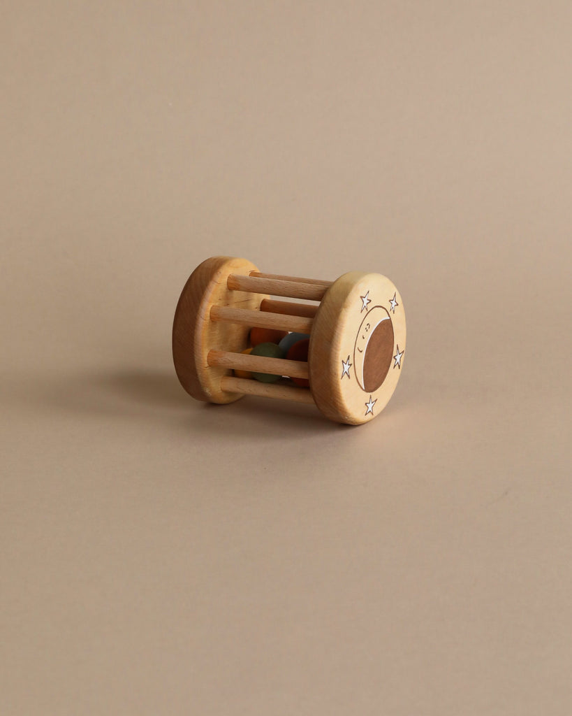 A Handmade Wooden Rattle, crafted from sustainably harvested birch wood, lies on a beige background. It features a cylindrical shape with several vertical bars and small, colorful balls inside.