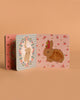 The Konges Sloejd Touch and Feel Book is a sturdy sensory board book with pastel rabbit, flower, and heart designs on a soft peach background. One bunny features a fuzzy area for tactile fun.