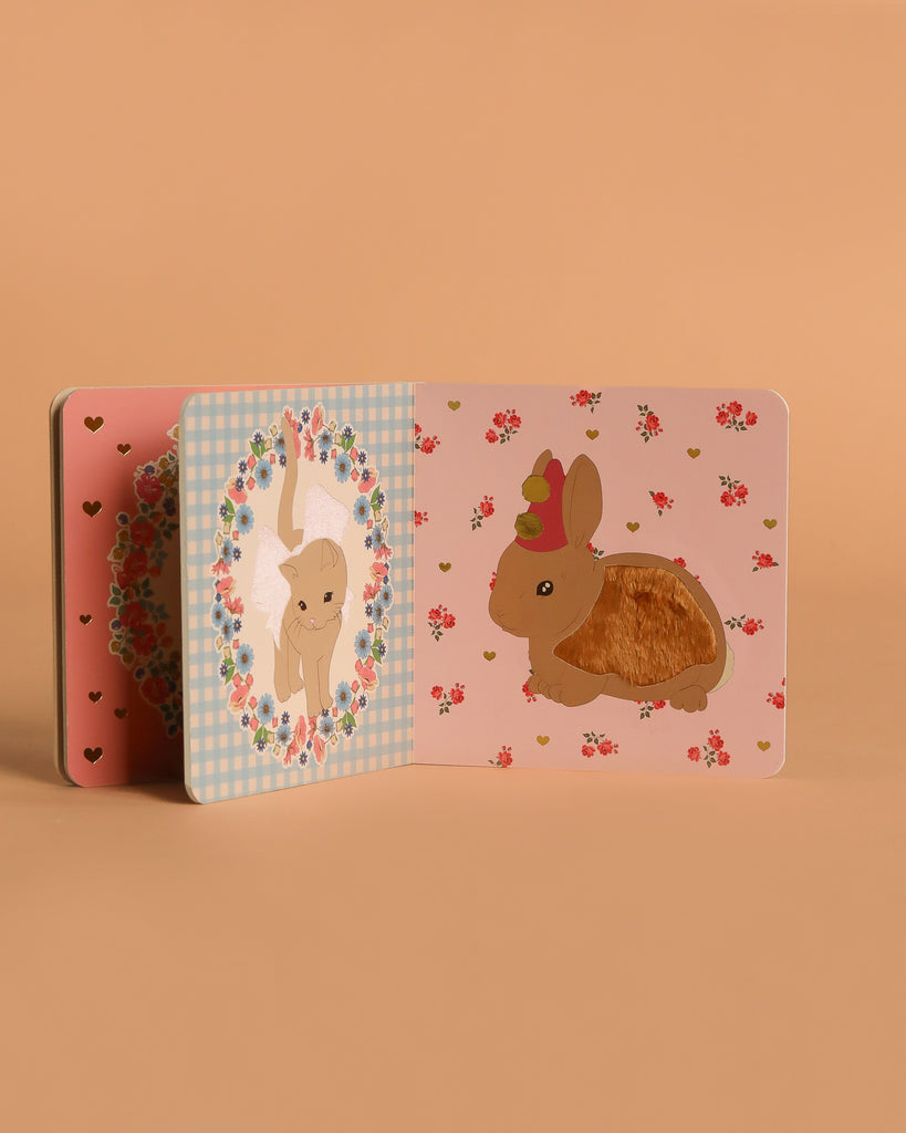 The Konges Sloejd Touch and Feel Book is a sturdy sensory board book with pastel rabbit, flower, and heart designs on a soft peach background. One bunny features a fuzzy area for tactile fun.