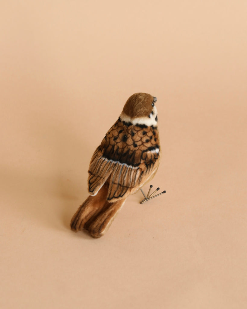 A small ceramic figurine of a Sparrow Bird Stuffed Animal perched on a branch, depicted with realistic features and colors, set against a plain, light beige background.