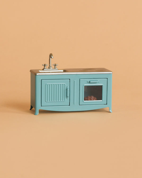 The Maileg Kitchen, Mouse - Blue is a small, blue vintage-style metal toy set with a sink, cabinet, and oven—complete with a windowed oven door showing a tiny item inside. Perfect for imaginative play with your mouse family.