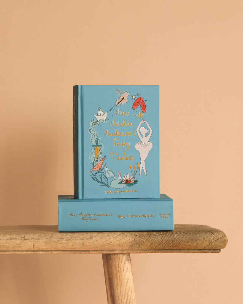 Two blue hardcover copies of "Hans Christian Andersen Fairy Tales | Collector's Edition" with whimsical illustrated covers are stacked on a wooden bench—one upright, one flat—against a light beige background.