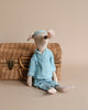 Maileg Maxi Mouse in Pyjamas, your perfect rest-time companion, is dressed in a blue striped pajama set with a matching nightcap. Seated against a wicker basket with a clasp, this charming stuffed toy stands out beautifully against the plain light beige background.